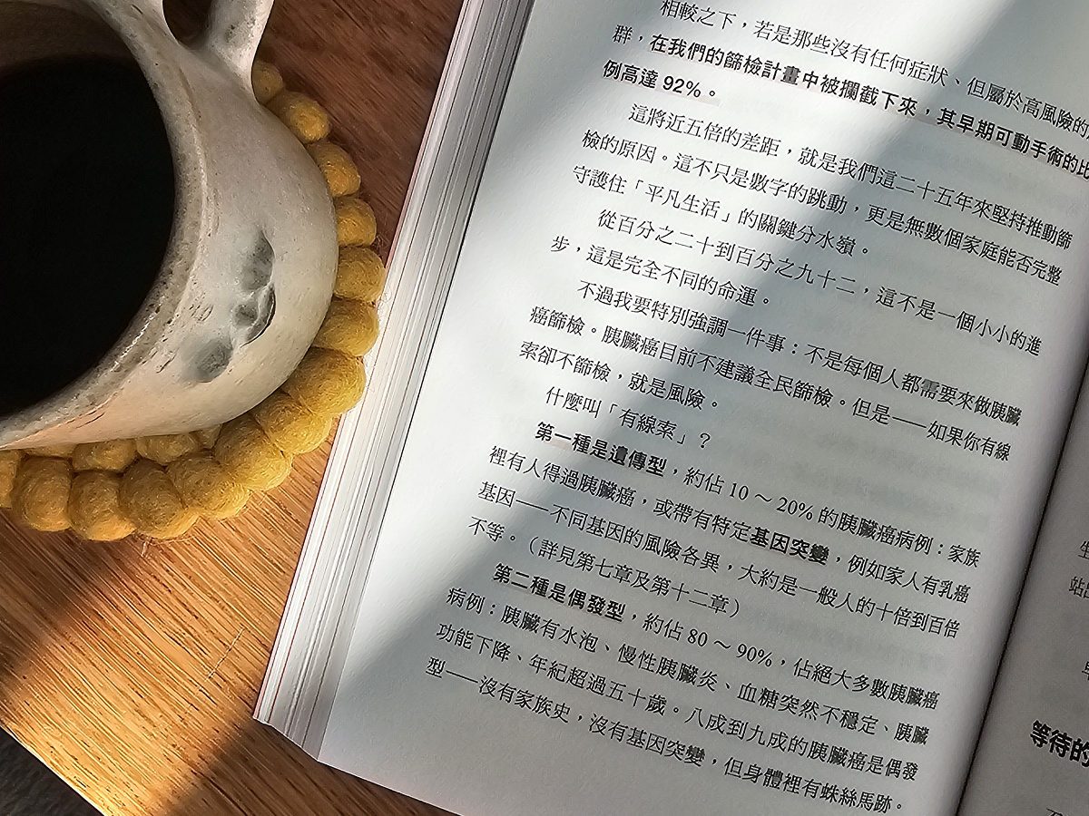 陽光下攤開的《攔截胰臟癌》書頁，內容談論胰臟癌篩檢與高風險族群的比例差距，一旁擺著白色陶杯。